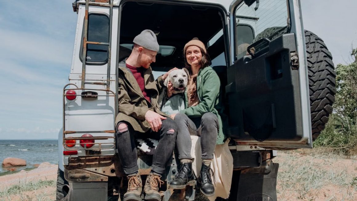 Young couple relaxing by the ocean in a van with their dog on a sunny day.